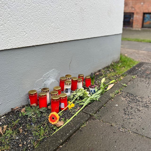 Blumen und Kerzen liegen einen Tag nach dem Tötungsdelikt an einem 23-jährigen Mann auf dem Gehweg der Moses-Heß-Straße in Köln-Stammheim