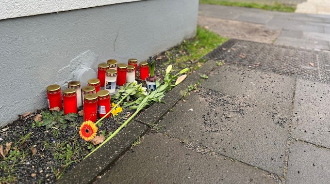 Blumen und Kerzen liegen einen Tag nach dem Tötungsdelikt an einem 23-jährigen Mann auf dem Gehweg der Moses-Heß-Straße in Köln-Stammheim