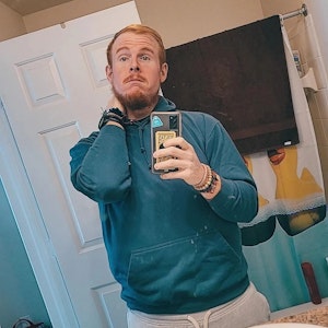 Casey King posiert vor einem Spiegel für ein Selfie. Er trägt einen blauen Kapuzenpullover.