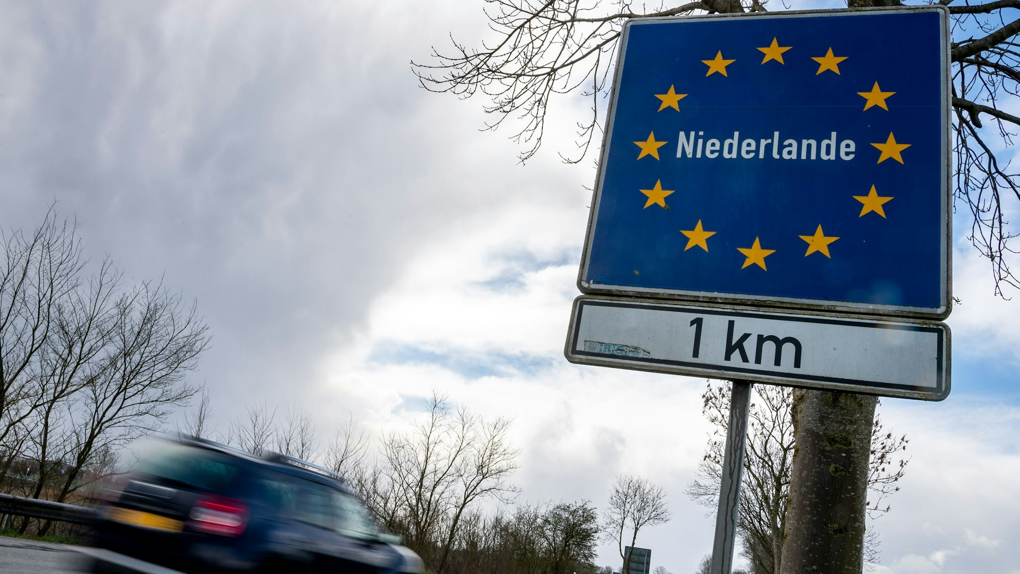 Ein Pkw fährt an einem Schild vorbei, das auf die deutsch-niederländische Grenze hinweist.