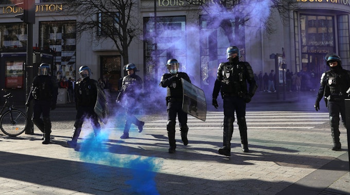 Frankreich, Paris: Polizisten gehen auf der Avenue des Champs-Elysees durch sich ausbreitendes Tränengas.