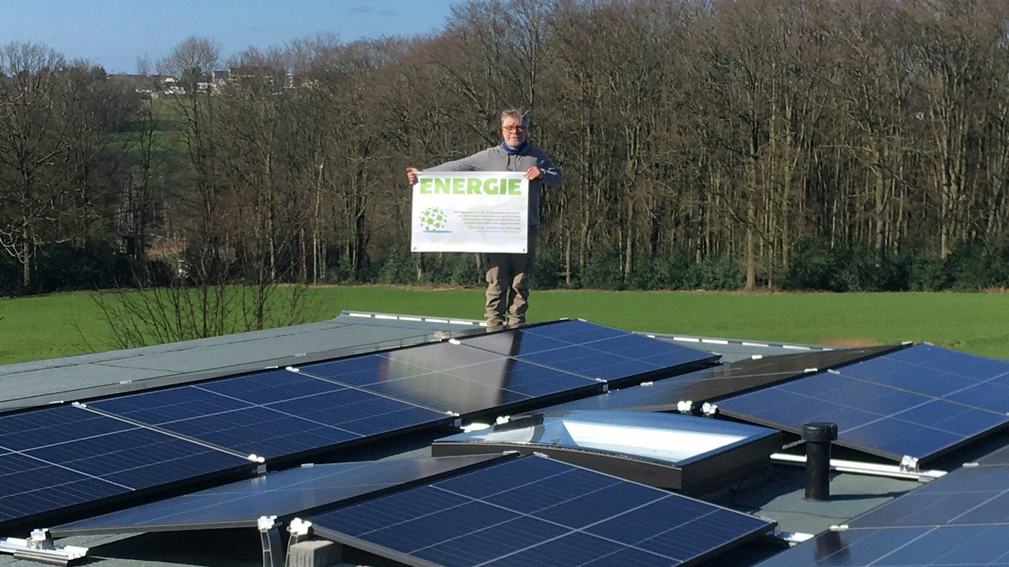 Stefan Häusler, Vorsitzender der Klimafreunde Rhein-Berg, steht auf einer Fotovoltaikanlage und hält ein Schild mit der Aufschrift „Energie“.