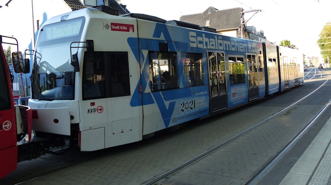 Durch eine Frechener Straße fährt eine KVB-Straßenbahn der Linie 7 mit blau-weißem Schriftzug "Schalömchen Köln".