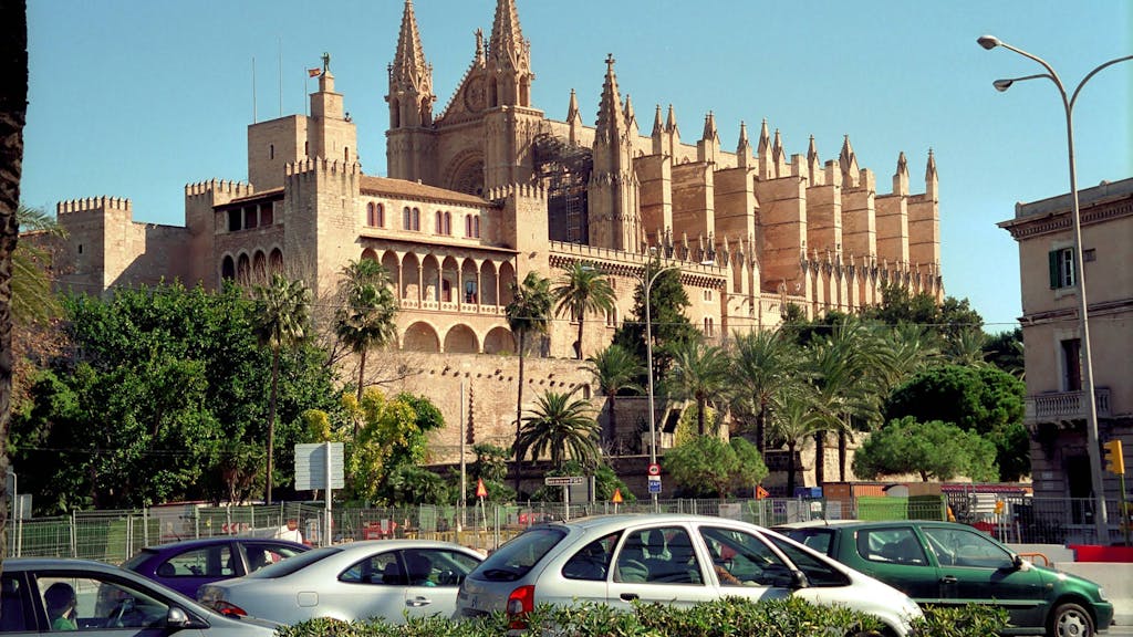 Autos stehen in Palma de Mallorca auf der Straße. Im Hintergrund: die Kathedrale La Seu.