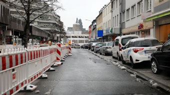 Links sind Baustellenbaken an der Schloßstraße zu sehen, rechts der freien Fahrbahn stehen parkende Autos. Geradeaus in die Schlossgalerie zu sehen.