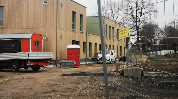 An einem Bauzaun vorbei ist ein zweistöckiges Gebäude mit einer Front aus Holz zu sehen. Die Kindertagesstätte soll im Sommer eröffnet werden.