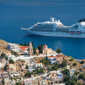 Ein Kreuzfahrtschiff fährt an einem griechischen Dorf vorbei.