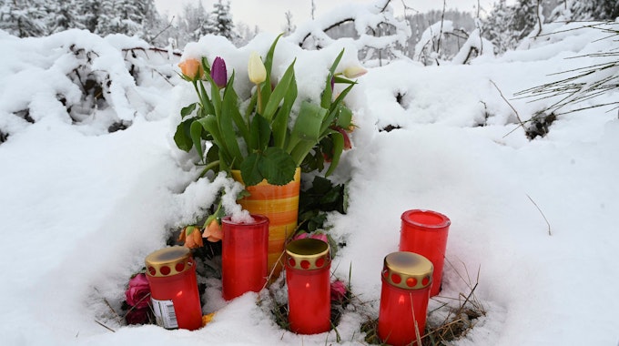 Grabkerzen und ein Tulpenstrauß stehen im Schnee, an dem Fundort des ermordeten zwölfjährigen Mädchens Luise.