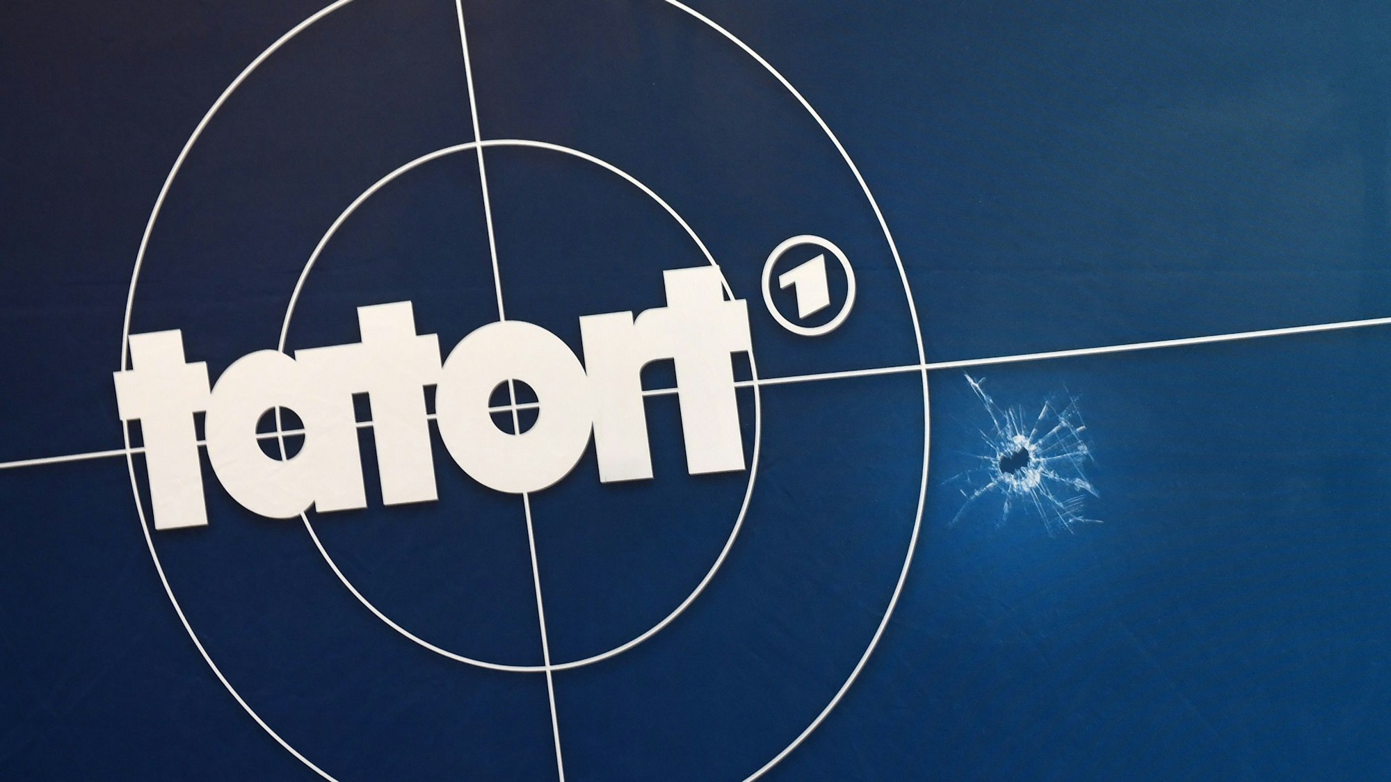 Auf einer Fotorückwand sind das Logo der ARD-Fernsehreihe „Tatort“, Einschusslöcher und Absperrband abgebildet.