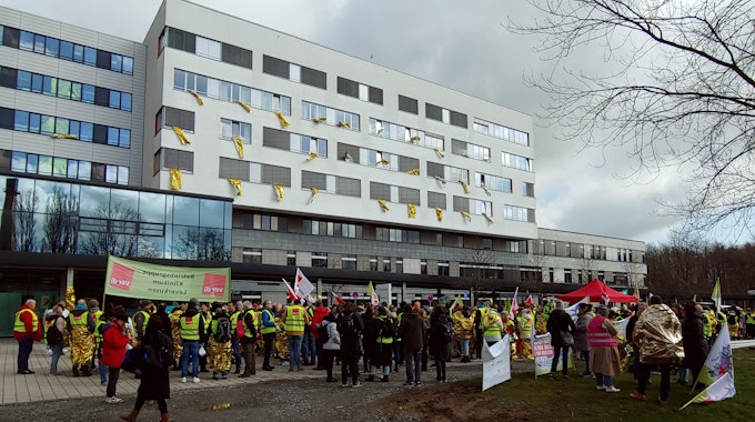 Menschen in Warnwesten und mit Protestschildern vor einem Krankenhausgebäude