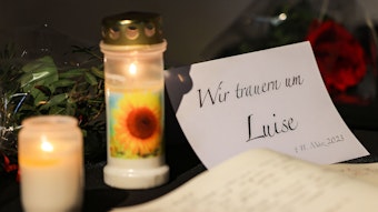 Zwei Kerzen und eine Trauerkarte stehen auf einem Tisch.