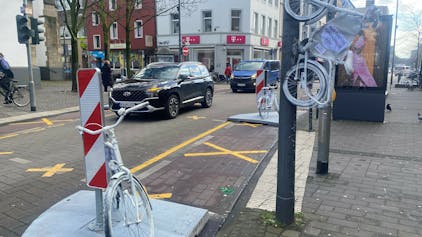 Auf der Venloer Straße stehen zwei weiße Fahrräder am Straßenrand, ein drittes hängt an einem Laternenmast.&nbsp;