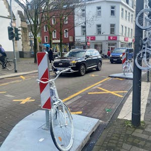 Auf der Venloer Straße stehen zwei weiße Fahrräder am Straßenrand, ein drittes hängt an einem Laternenmast.&nbsp;