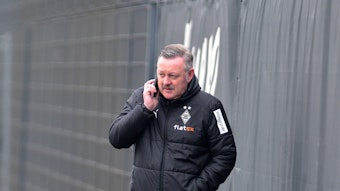 In Gesprächen: Borussia-Manager Roland Virkus telefoniert auf dem Trainingsplatz von Borussia Mönchengladbach während einer Einheit am 9. März 2023. Das Foto zeigt Virkus in einer Gladbach-Winterjacke und mit einem Telefon am rechten Ohr.