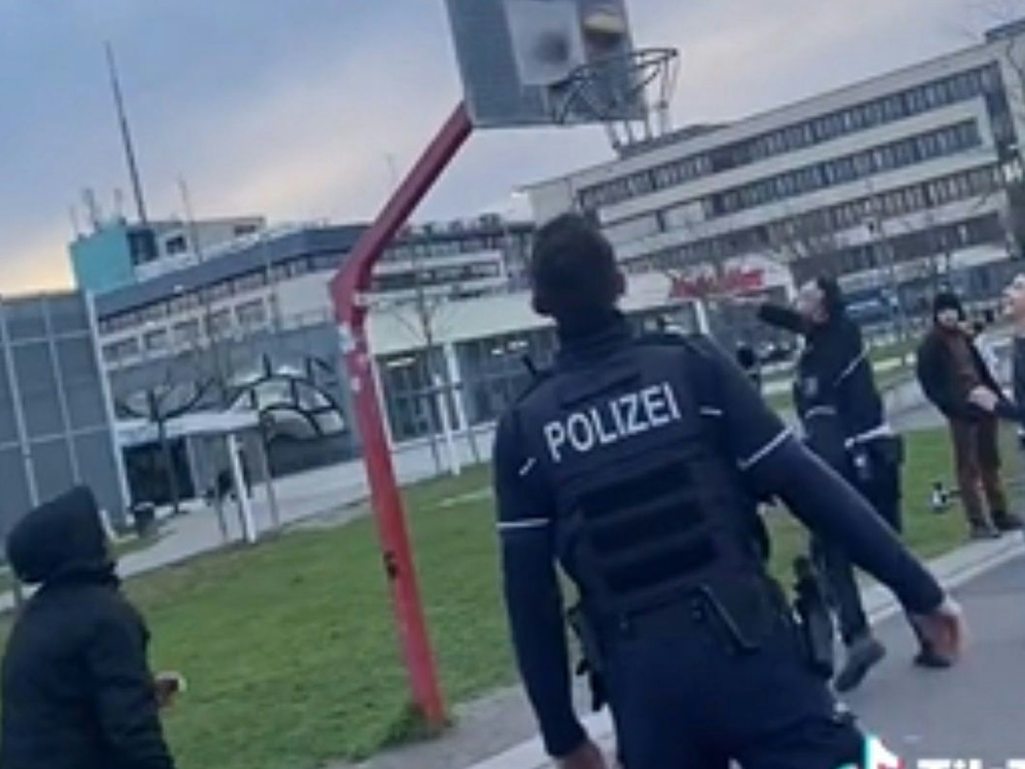 Zwei Polizisten spielen mit Kindern und Jugendlichen Basketball, ein Beamter wirft gerade einen Korb.