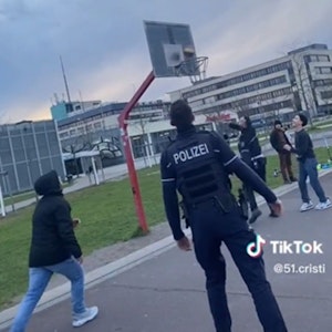 Zwei Polizisten spielen mit Kindern und Jugendlichen Basketball, ein Beamter wirft gerade einen Korb.