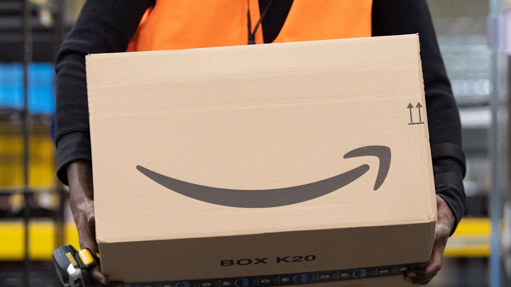 Ein Sortiermitarbeiter von Amazon trägt in einem Verteilzentrum ein Paket.