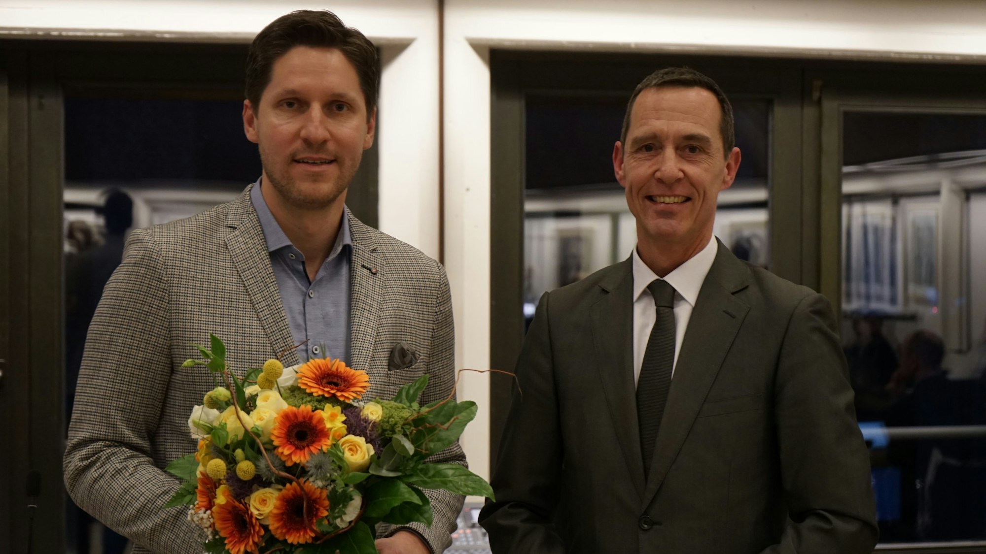 Dominik Laufs (links) ist vom Rat der Kolpingstadt zum Ersten Beigeordneten ernannt worden. Er hält einen Strauß Blumen in der Hand.