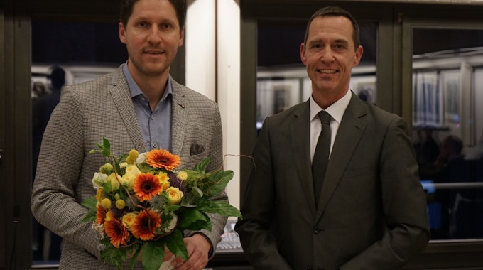 Dominik Laufs (links) ist vom Rat der Kolpingstadt zum Ersten Beigeordneten ernannt worden. Er hält einen Strauß Blumen in der Hand.