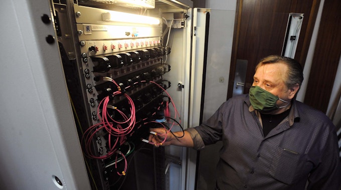 Jörg Brauckhoff steht mit Maske an der geöffneten Türe des Schaltschranks im Serverraum