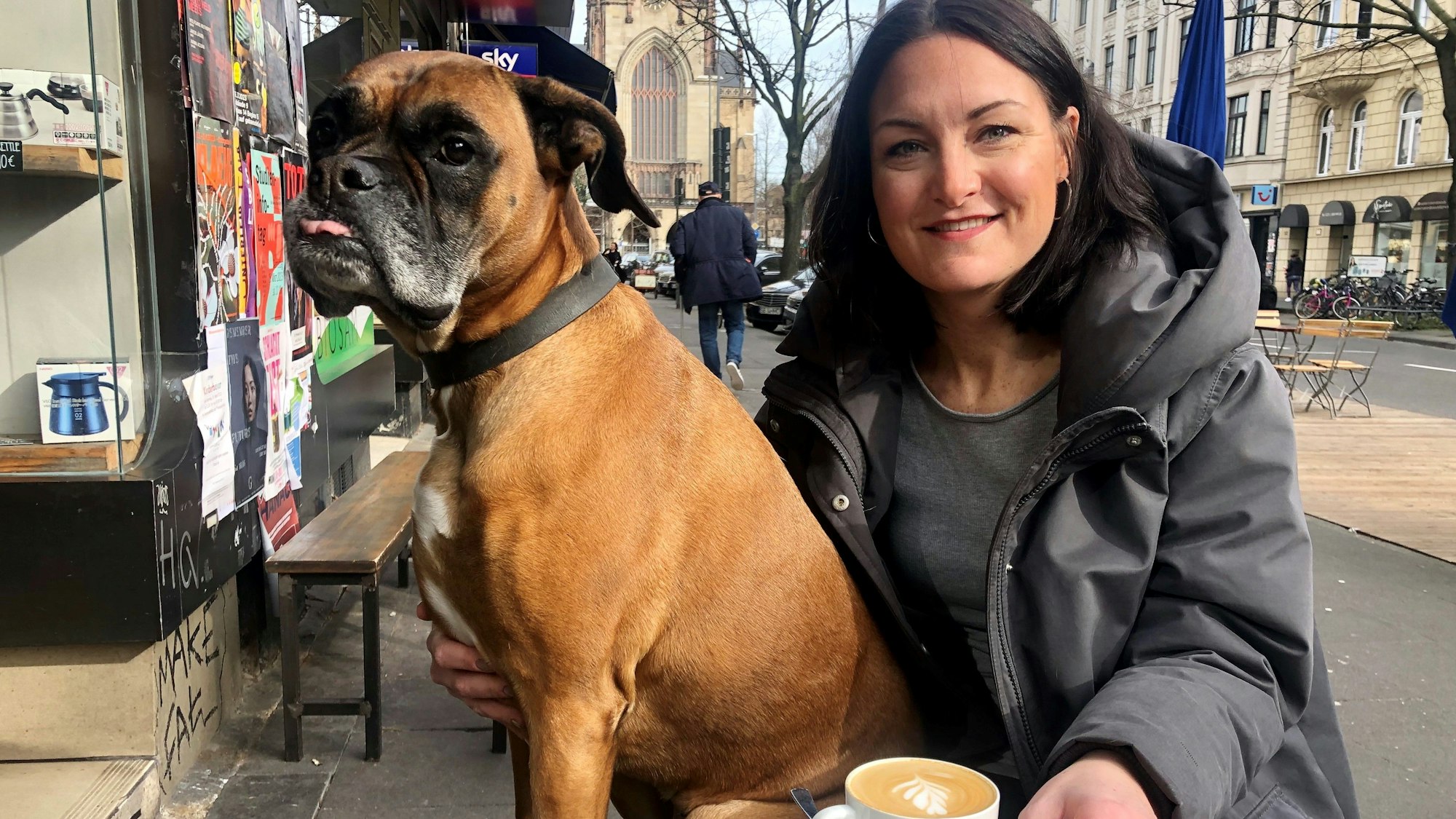 Junge Frau mit Boxer an einem Cafe draußen.