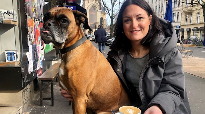 Junge Frau mit Boxer an einem Cafe draußen.