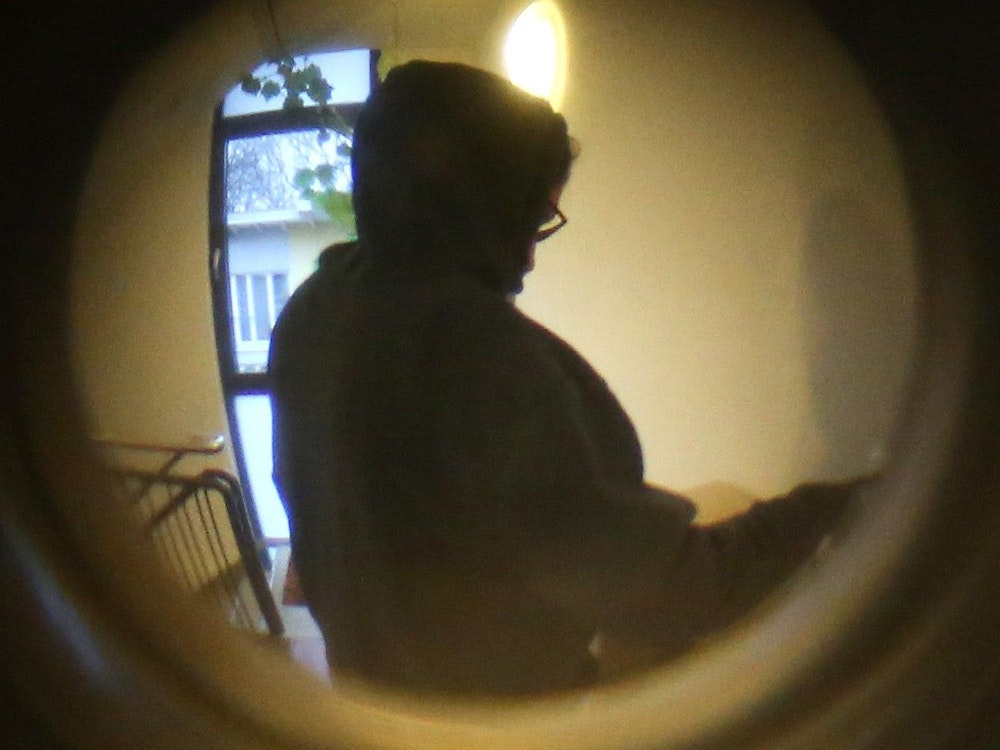 Durch einen Türspion ist eine Person mit einem Kapuzenpulli vor einer Wohnungstür zu sehen. Die Kölner Polizei sucht einen Mann, der möglicherweise am Tat-Tag einen schwarzen Kapuzenpullover trug. Das Foto steht in keinem Zusammenhang mit den aktuellen Vorkommnissen in Leverkusen.