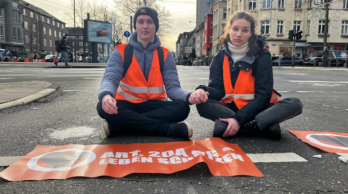 Ein Aktivist und eine Aktivistin sitzen Hand in Hand auf der Straße in Köln.