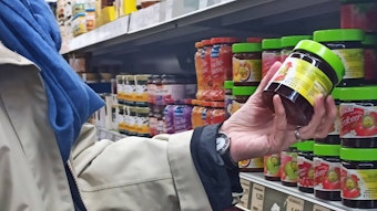Eine Kundin hält in einem Supermarkt ein Glas Marmelade in der Hand. Im Hintergrund sind auch Produkte der Eigenmarke von „Edeka“ zu sehen.