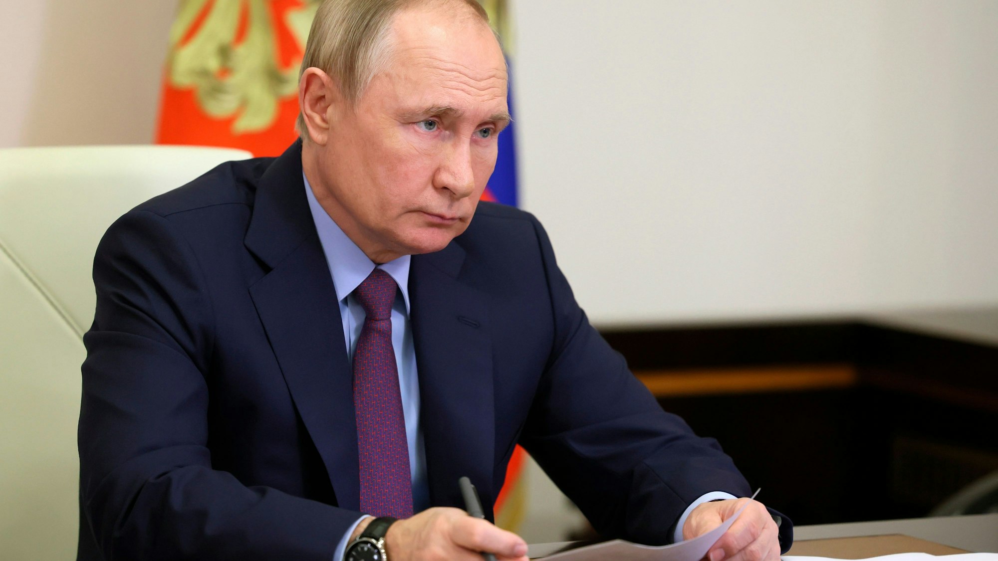 Putin sitzt an einem Tisch und hält ein Blatt Papier.
