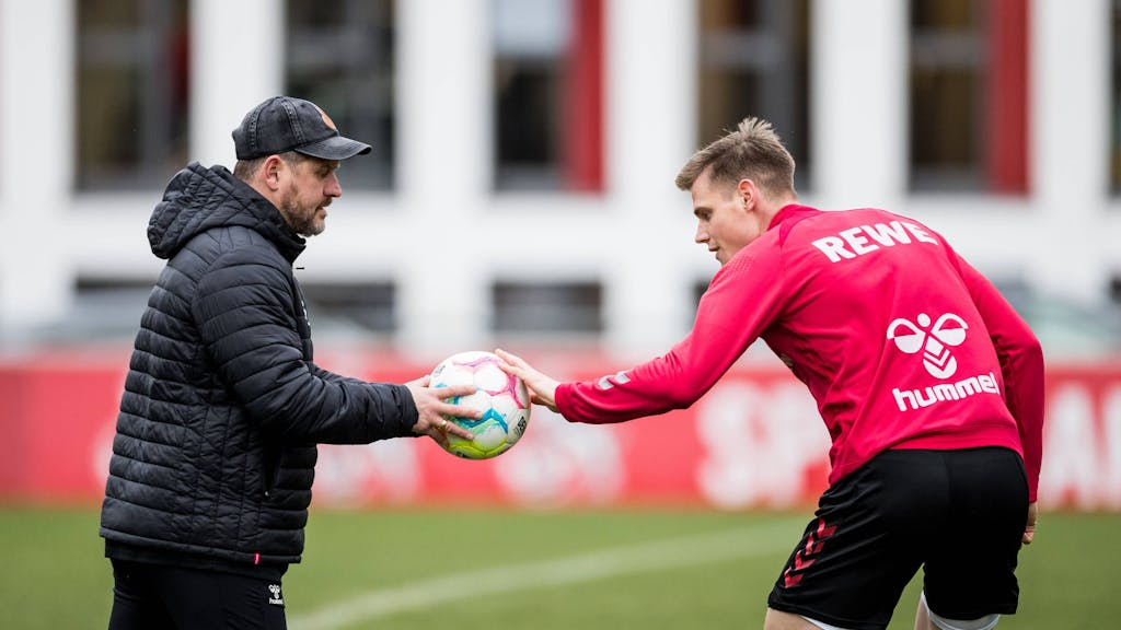 Steffen Tigges hält Steffen Baumgart im Training des 1. FC Köln einen Ball hin.