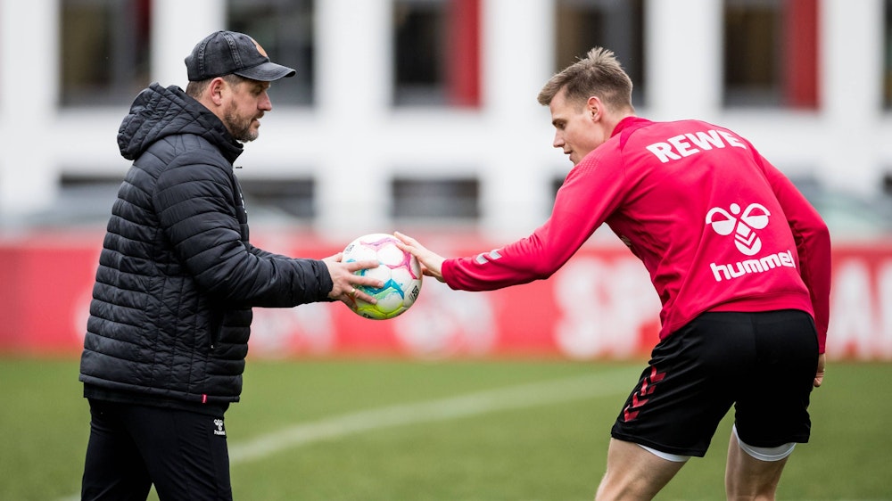 Steffen Tigges hält Steffen Baumgart im Training des 1. FC Köln einen Ball hin.