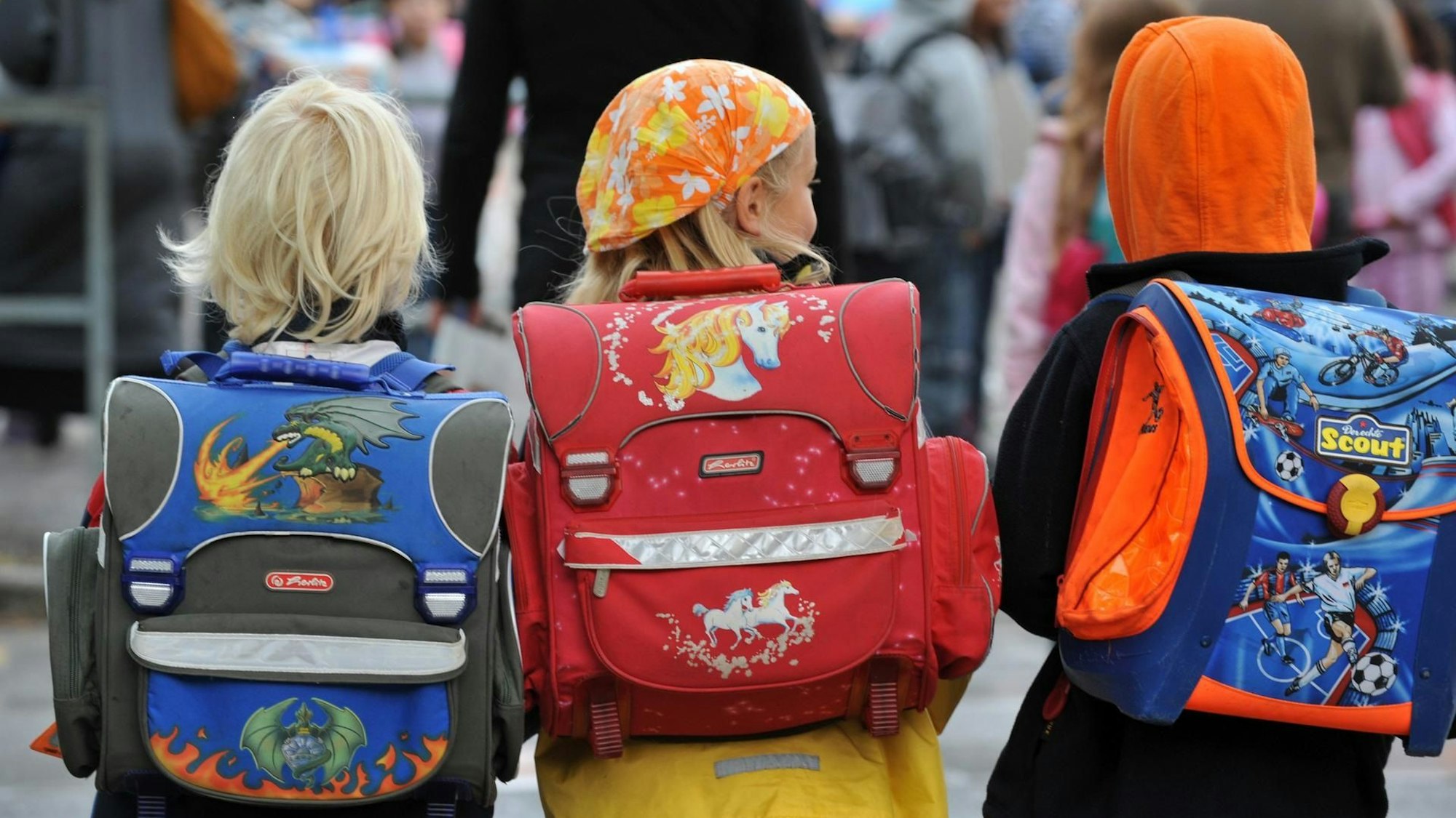 Drei Kinder laufen mit ihren Schulranzen zur Schule.