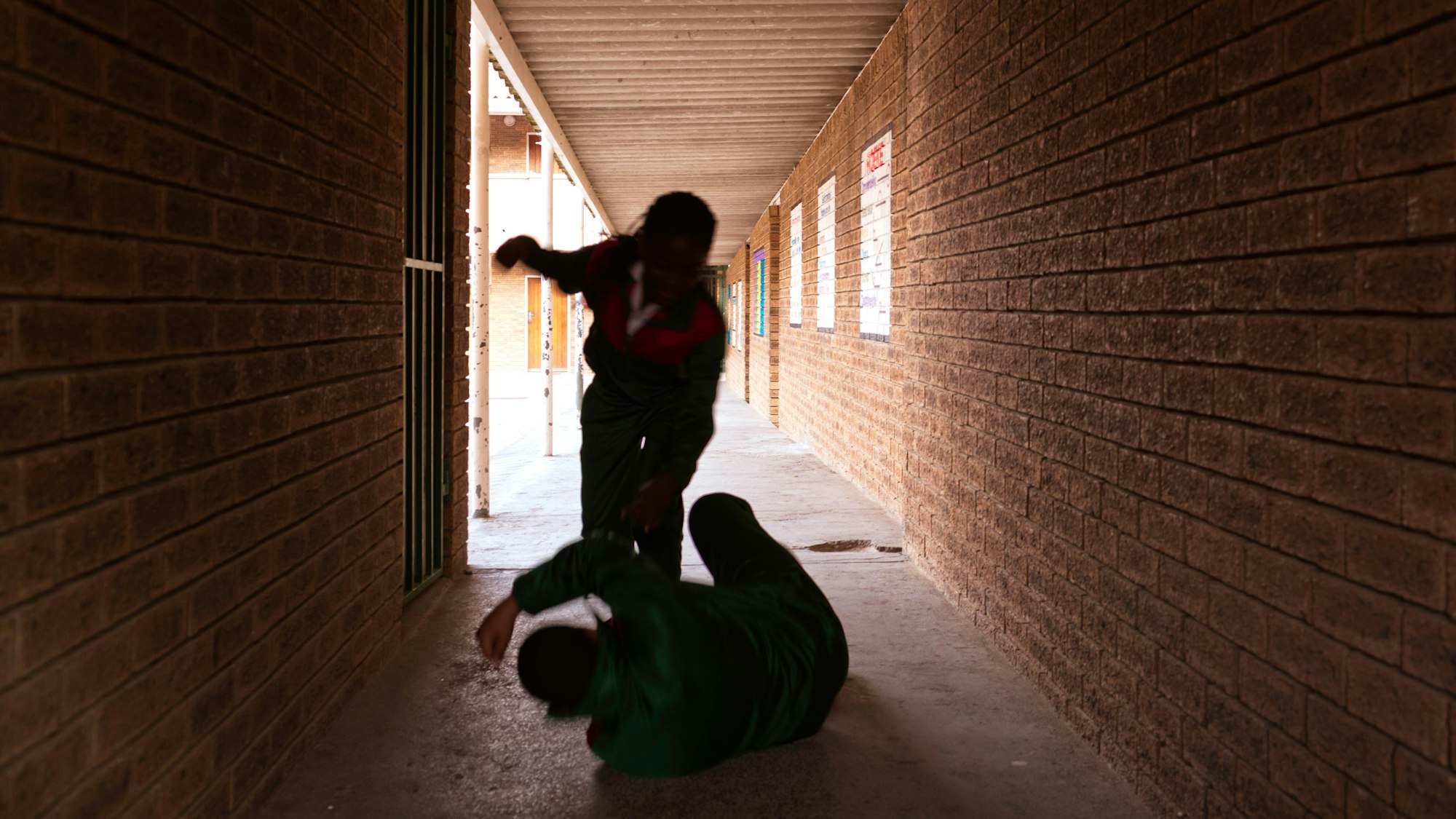 Zwei Mädchen kämpfen auf einem überdachten Gang in einer Schule.