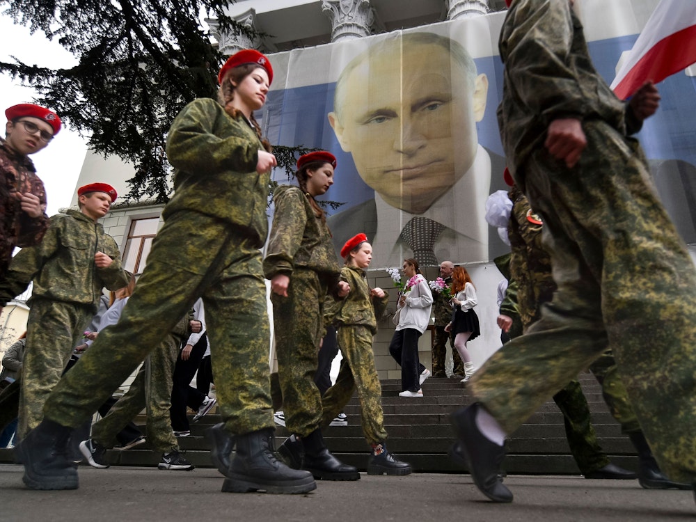 Uniformierte Jugendliche marschieren anlässlich einer Aktion zum neunten Jahrestag der Krim-Annexion an einem Bildnis des russischen Präsidenten Wladimir Putin (im Hintergrund) vorbei.