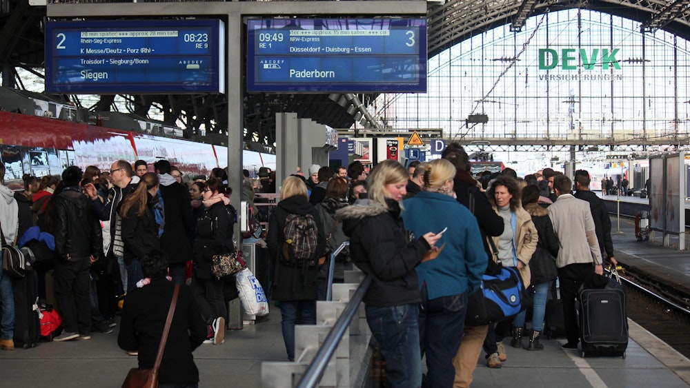 Viele Menschen stehen mit Koffern an den Gleisen am Hauptbahnhof in Köln und warten.
