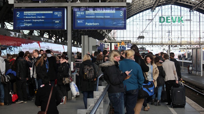 Viele Menschen stehen mit Koffern an den Gleisen am Hauptbahnhof in Köln und warten.