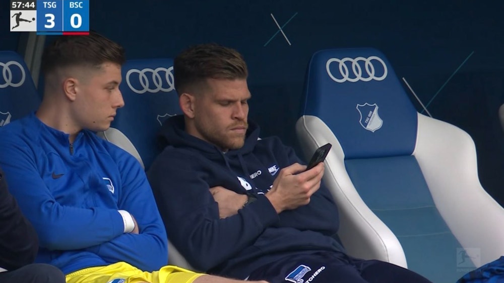Florian Niederlechner sitzt auf der Bank schaut während des Spiels von Hertha BSC bei der TSG Hoffenheim auf sein Handy.