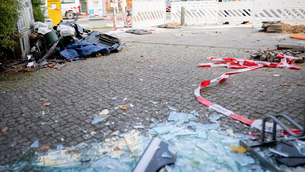 Glassplitter einer zerstörten Fensterscheibe liegen auf dem Boden, daneben Flatterband der Polizei.