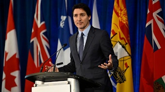 Justin Trudeau, Premierminister von Kanada, steht an einem Podium, hinter ihm mehreren Fahnen.