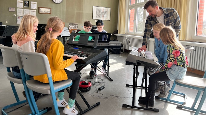 Musiklehrer zeigt Grundschulkindern in der Musikschule Leverkusen, wie Tasteninstrumente bedient werden.
