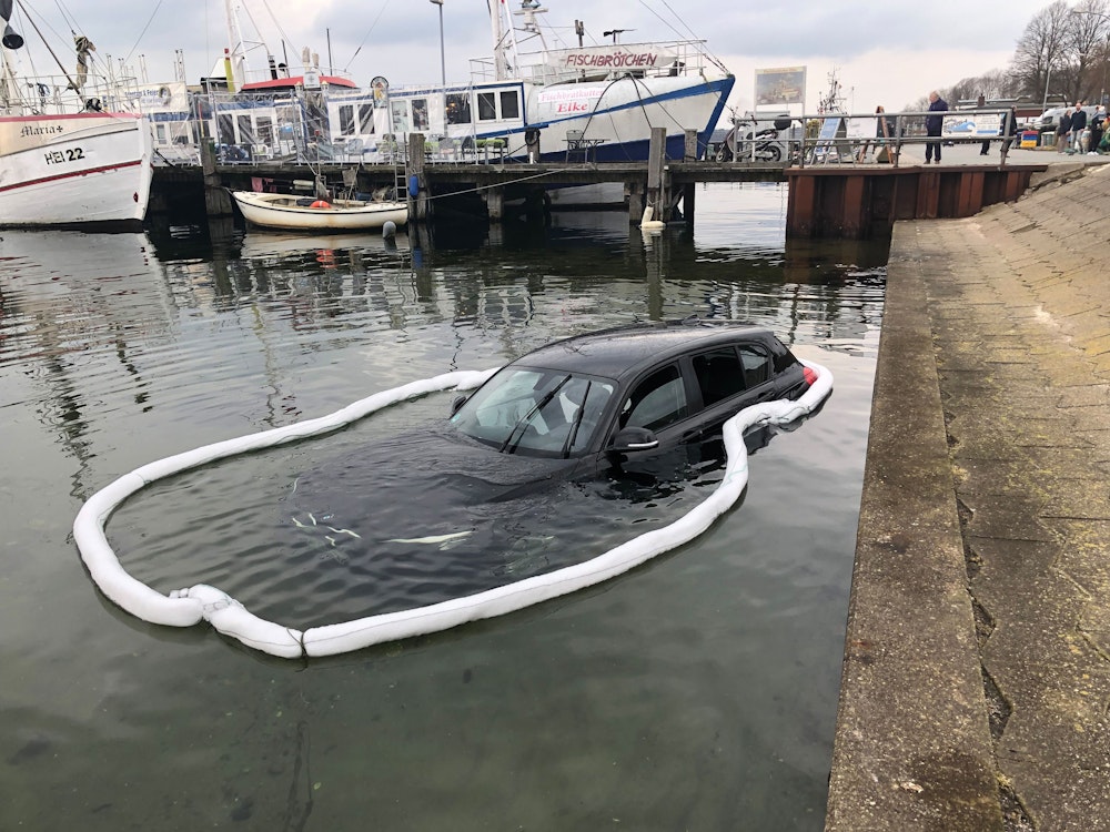 Ein Auto steht im Hafenbecken halb unter Wasser, umgeben von einer Ölsperre gegen möglicherweise austretende Schmierstoffe. Der Mann, der den Wagen ins Hafenbecken gesteuert hatte und dem von Passanten aus dem Fahrzeug geholfen wurde, blieb unverletzt.