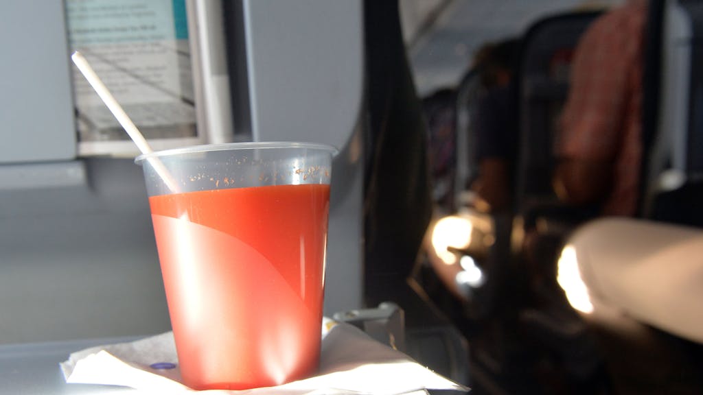 Ein Plastikbecher mit Tomatensaft steht auf dem Flug nach Berlin auf dem Klapptisch im Flugzeug.&nbsp;