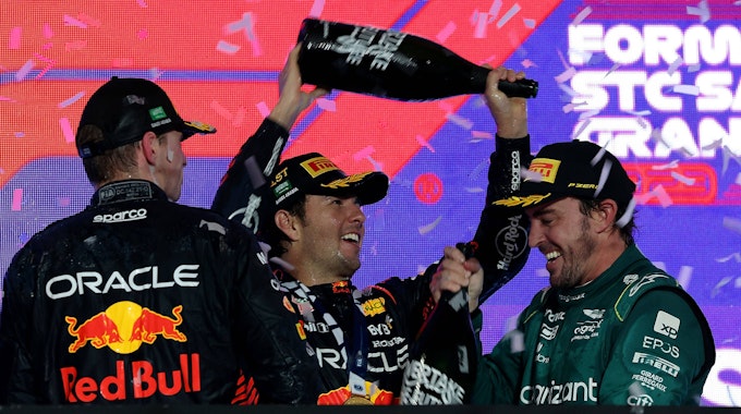 Sergio Perez schüttet Fernando Alonso Champagner über den Kopf, Max Verstappen schaut zu.