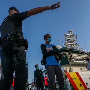 Flüchtlinge verlassen ein Schiff. Ein Mann zeigt ihnen die Richtung, in die sie gehen sollen.