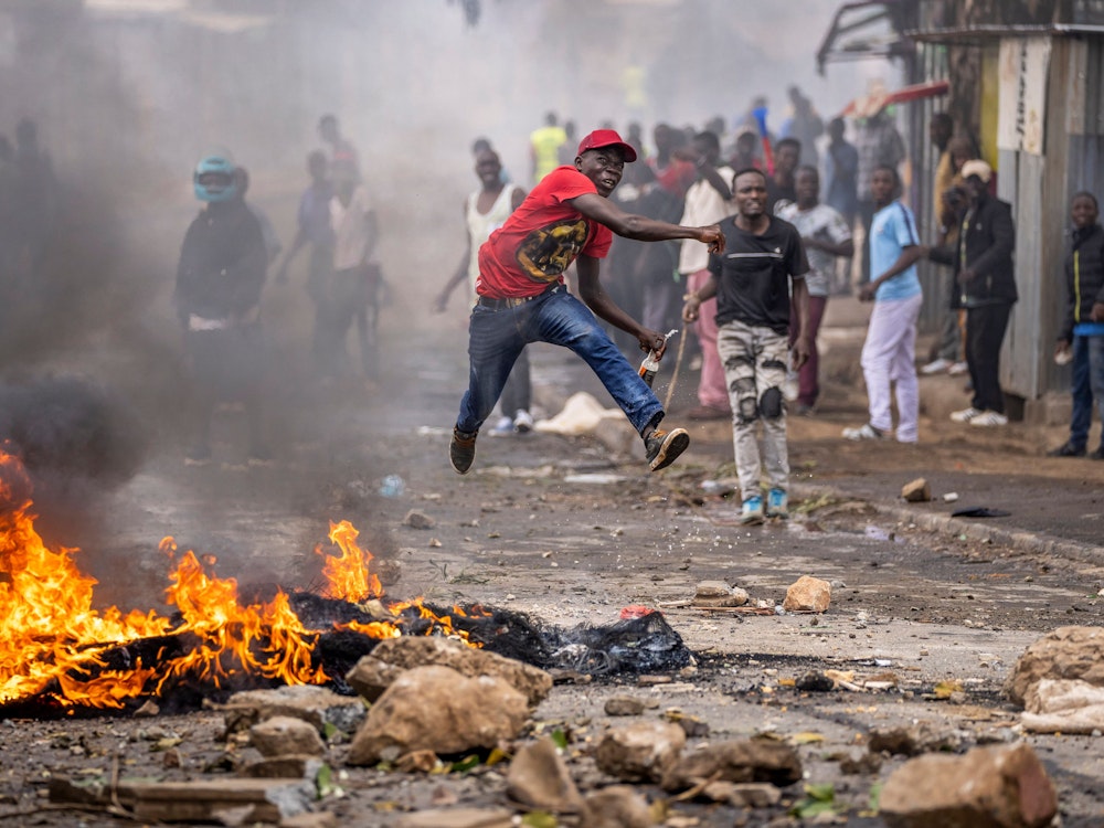 Ein Demonstrant springt in die Luft, als er einen Stein neben einer brennenden Barrikade im Kibera-Slum in Nairobi (Kenia) in Richtung der Polizei wirft.