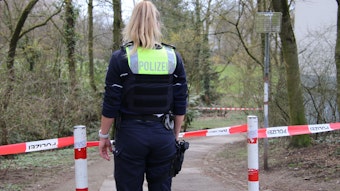 Eine Polizistin steht vor einem Absperrband im Weidenpescher Park, wo ein Mann am Sonntag auf einen Spaziergänger und dessen Hund eingestochen hat.