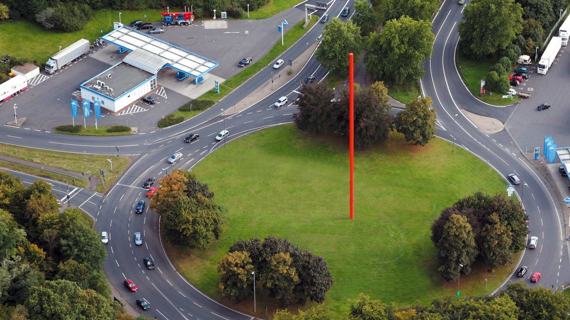 Auf einem begrünten Kreisverkehr steht eine rote Stange.
