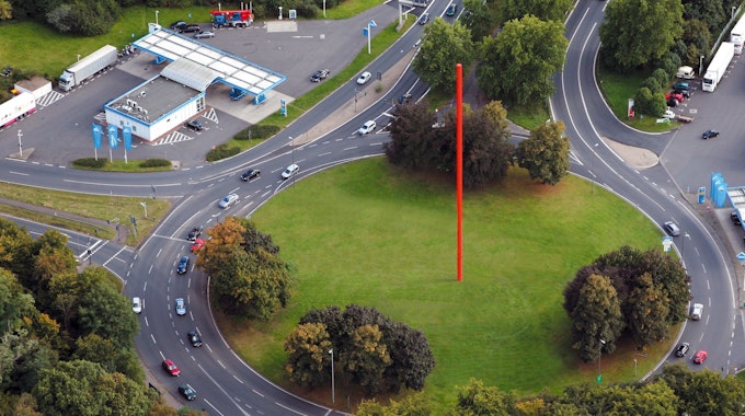 Auf einem begrünten Kreisverkehr steht eine rote Stange.