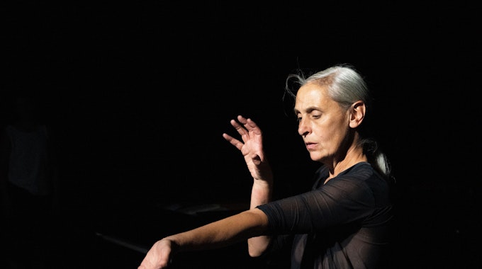 Die belgische Choreografin Anne Teresa De Keersmaeker tanzt „The Goldberg Variations, BMV 988“ in Köln. Den linken Arm hält sie ausgestreckt, mit der Handinnenfläche nach oben, den rechten Arm hat sie angewinkelt.